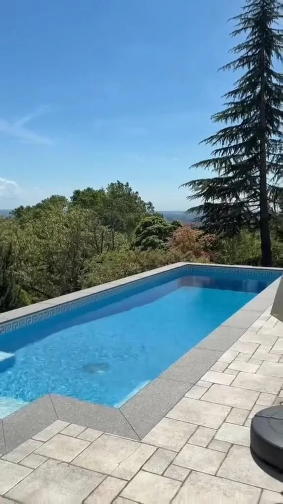Bazen s kamenim opločenjem u vrtu kuće s pogledom na brda
